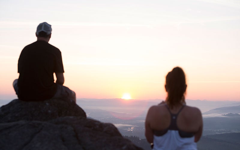 Two students watching the sunrise from the top of a mountain.