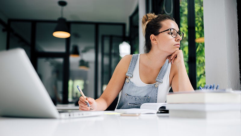 A student sits at a desk, distracted from her homework