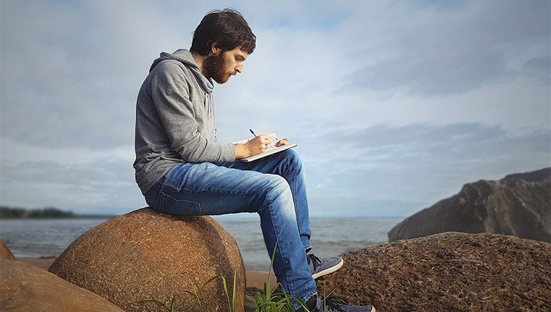 A man writes in a journal by the ocean